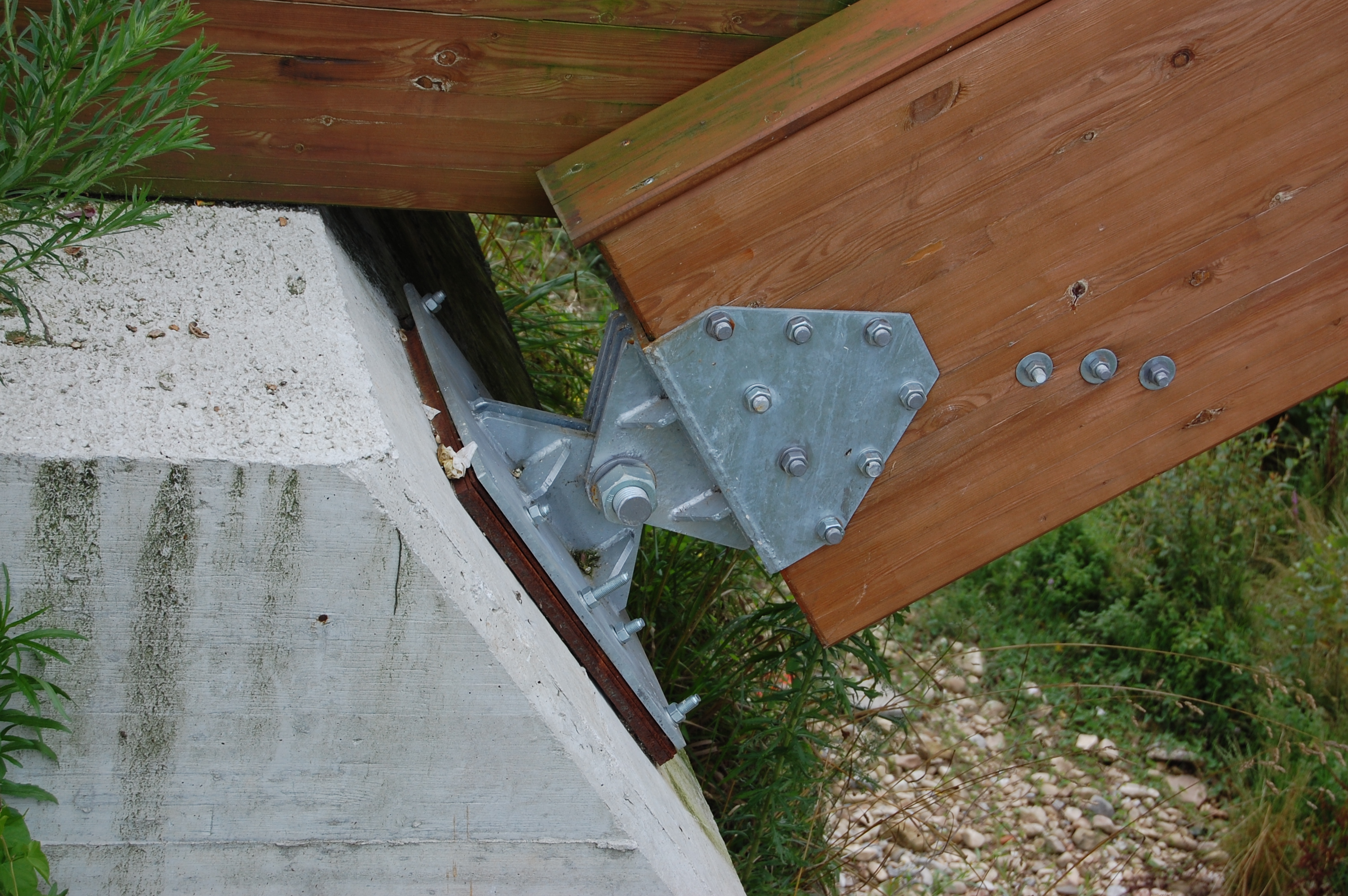 Foto de detalle de un apoyo articulado fijo en la base de un puente de madera.