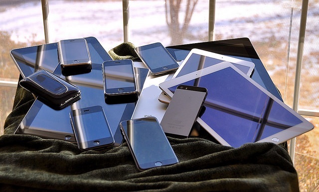 Grupo de dispositivos móbiles de diferentes tipos sobre unha mesa nunha paisaxe exterior.