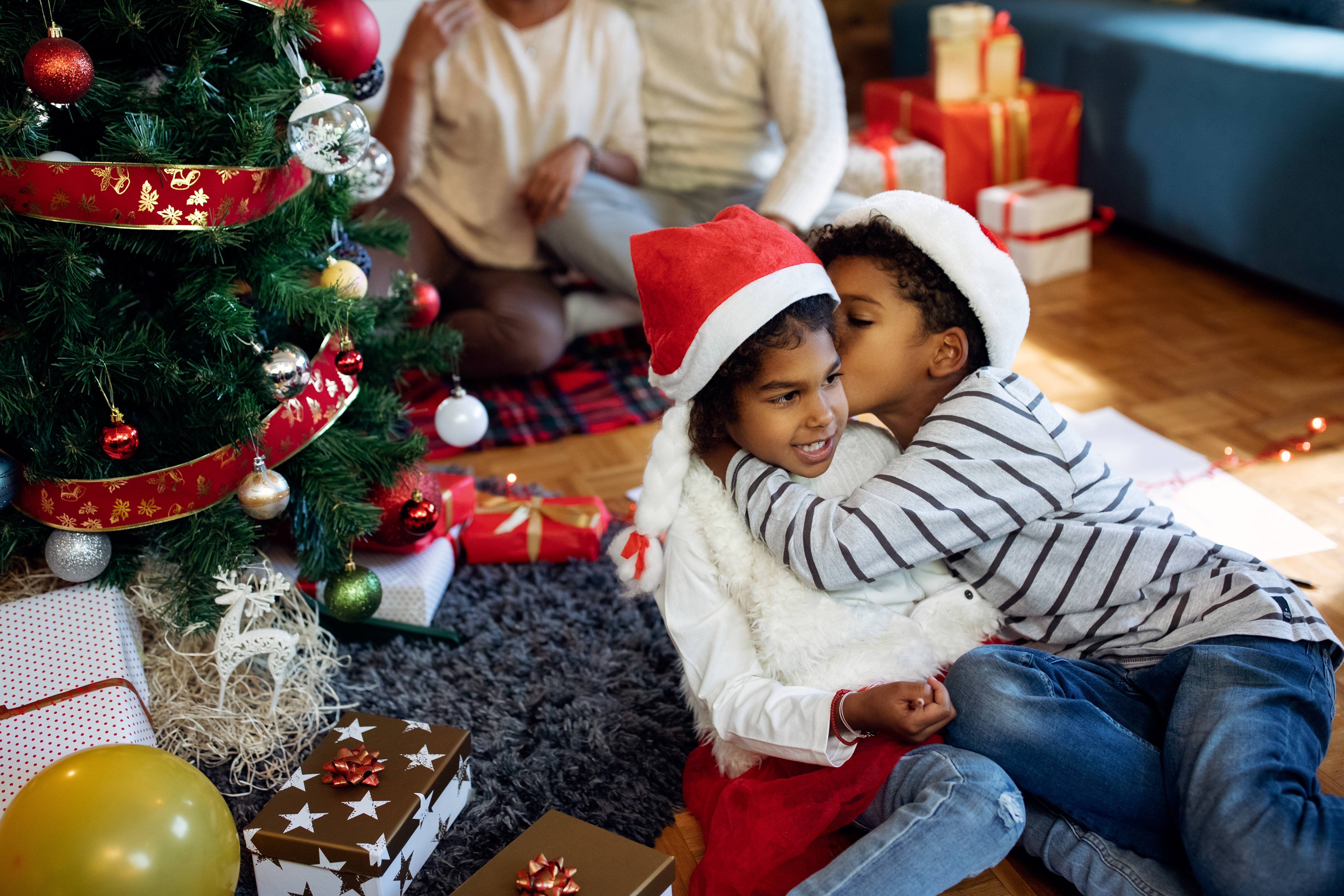 Sibligs hugging under a Christmas tree.