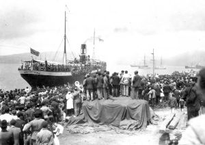 Zarpar Imagen no relevante para la comprensión del texto. Fotografía antigua de un puerto en el que está zarpando un barco y en el muelle la gente se despide