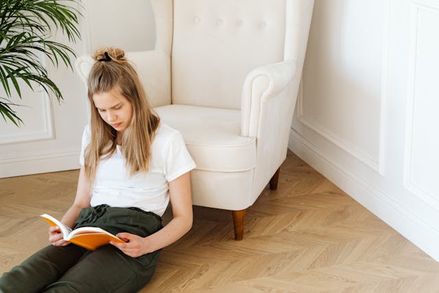 Niña sentada en el suelo concentrada leyendo un libro