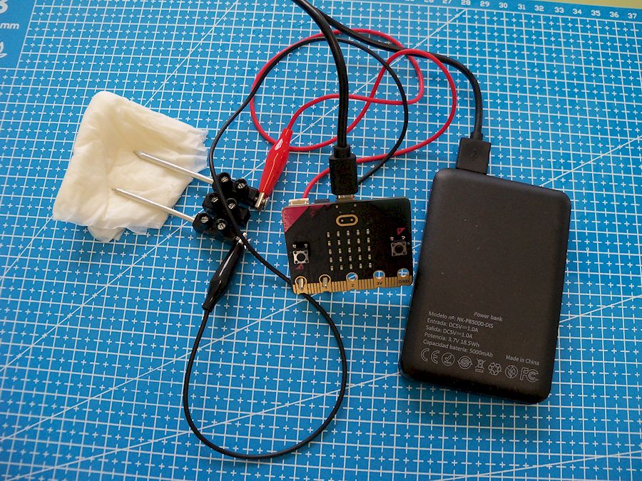 Placa Micro:Bit conectada a unha regreta con dous cravos apoiados nun papel mollado