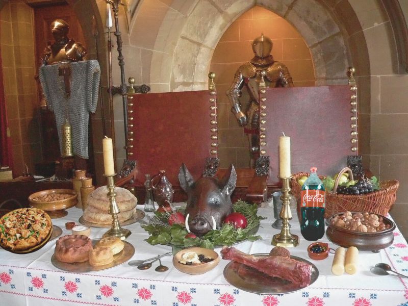 Móstrase unha imaxe dun banquete medieval con comida e bebida da época salvo por dous anacronismos,