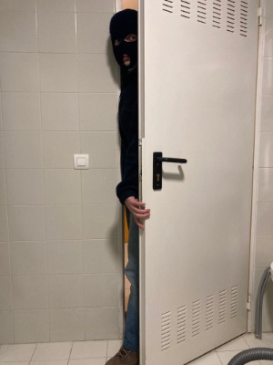 Ladrón con pasamontañas cerca de pared alicatada.