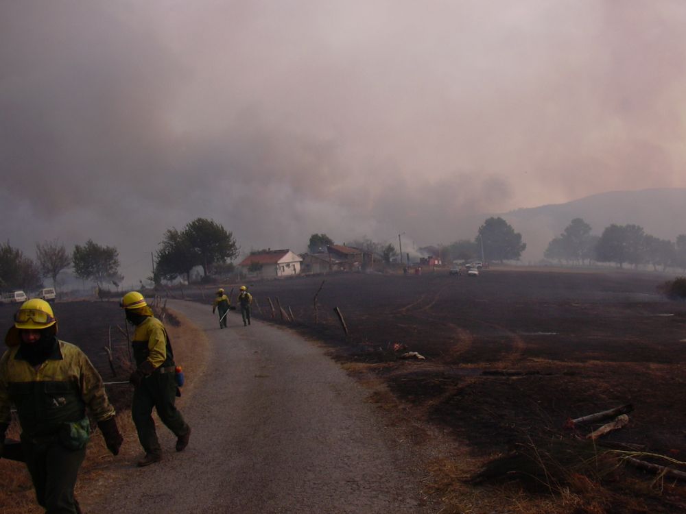 Medios de extinción actuando en un incendio con una casa al fondo.