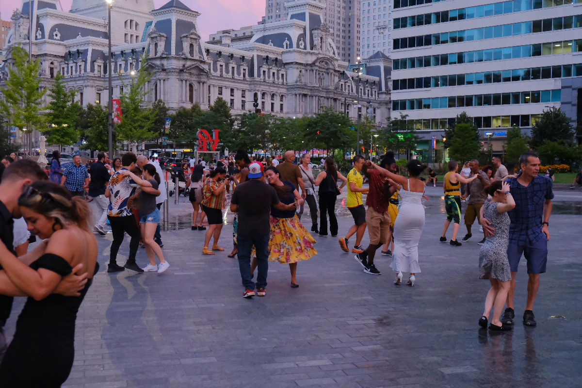Grupo de danzantes de salsa na rúa, bailando ao aire libre nun parque.