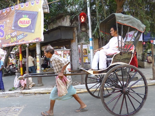 Fotografía dun medio de transporte tirado por unha persoa que consiste nun asento que se move sobre dúas rodas.