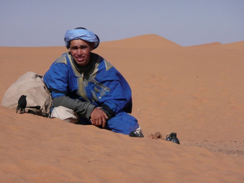 Imaxe dun Tuareg vestido de cor índio, sentado no deserto