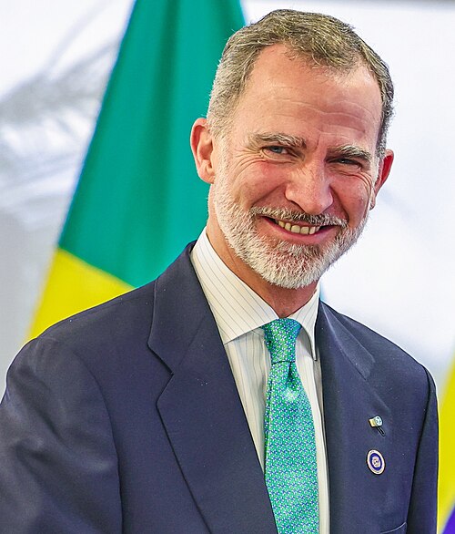 Imaxe de Filipe VI, sorrinte, vestido cun traxe azul mariño, unha camisa branca raiada, e unha gravata verde.