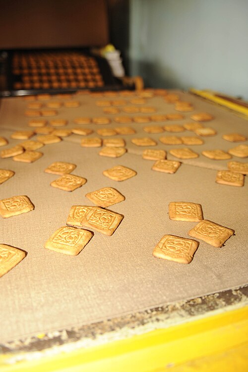 Cookies production in Bishkek, Kyrgyzstan (5) Galletas recién cocinadas salen de un horno industrial.