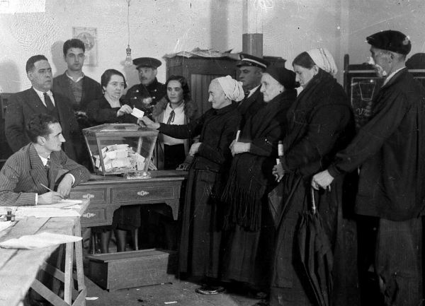 Eibar_1933 Una mesa electoral con la urna, preside una mujer. Varias mujeres y hombre preparados para votar.