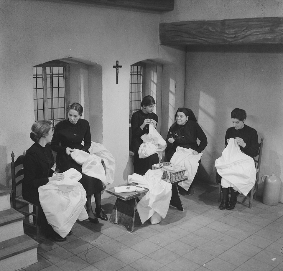 Cinco mujeres vestidas de negro, sentadas juntas y cosiendo.