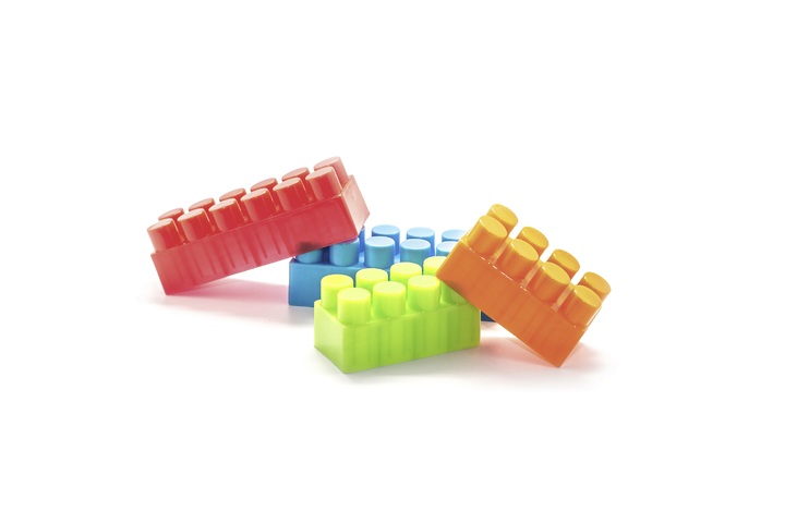 Fotografía de cuatro piezas de lego amontonadas sorbe un fondo blanco.Todas del mismo tamaño menos una roja que es más grande. El resto azul, verde y naranja.