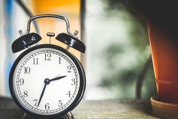 Reloj despertador con manecillas y números negros sobre fondo blanco.