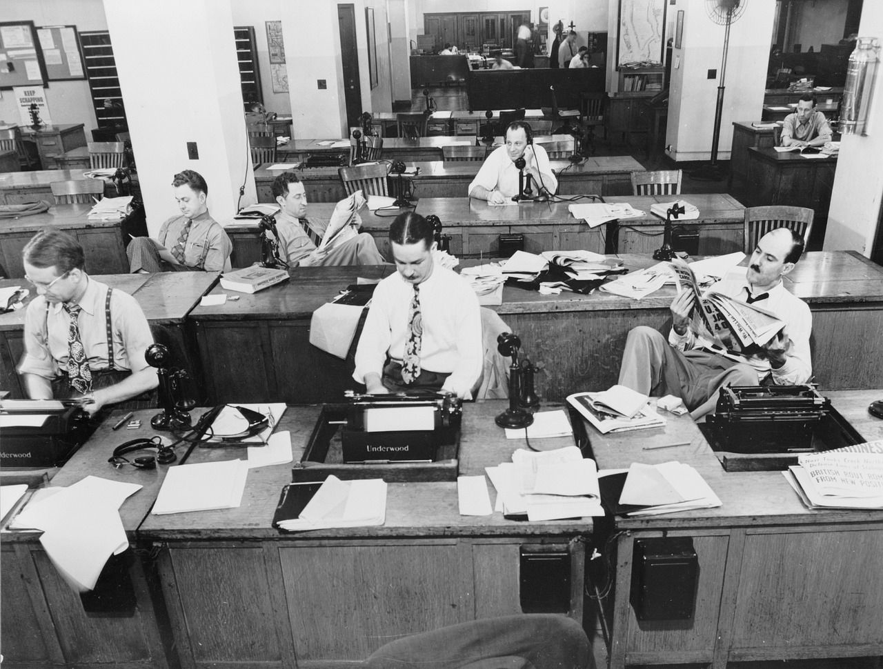 Fotografía en blanco y negro de la redacción de un periódico. Varias personas trabajando en sus mesas.