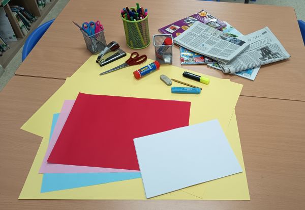 Imagen en la que se ven cartulinas, folios de colores, tijeras, pegamento, grapadora, rotuladores, periódicos y revistas viejas.