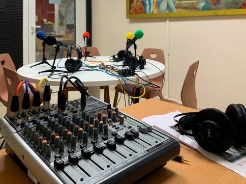 Mesa de mesturas dunha radio dun centro escolar cos micrófonos ao fondo. 