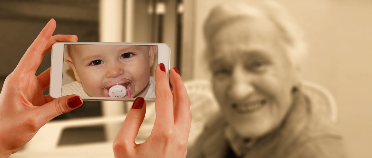 Mano sacando una foto con un móvil a una anciana que en el móvil se ve como un bebé.