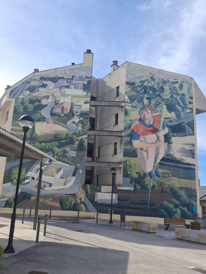 Mural de una anciana subiendo por el tronco de una berza con un huerto de fondo
