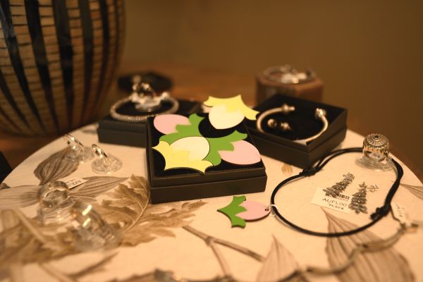 Cuatro broches de madera con forma de capullo de flor que encajan entre si. Están expuestos junto con joyas artesanales elaboradas en plata.
