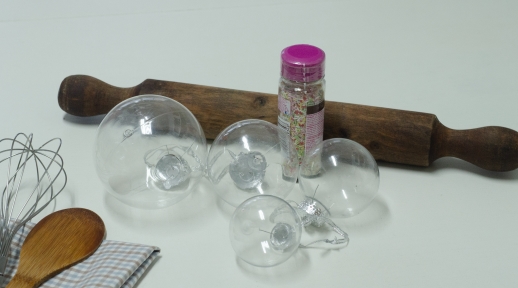 4 bolas de navidad transparentes de distintos tamaños y 2 botes cilíndricos llenos de pequeños fideos de caramelo de colores.