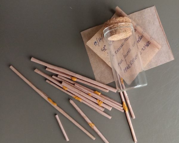 Rollos de papel de distintos tamaños y un cilindro de cristal con tapón de corcho.