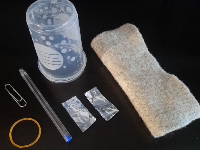 Imagen de un vaso de plástico, un bolígrafo, un clip, una goma elástica, papel de aluminio y un trapo.