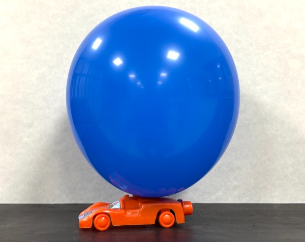 Coche de juguete naranja con un globo azul encima para que sea propulsado.