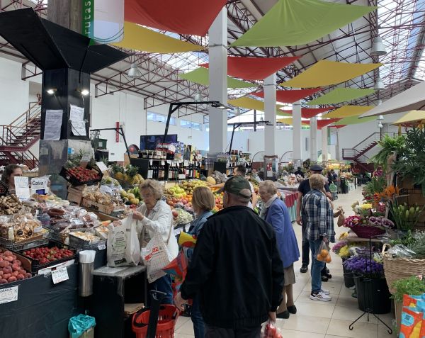 Personas comprando en un mercado con diferentes puestos de frutas y verduras.